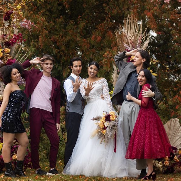 bride and groom posing with guests amidst fall foliage at their wedding