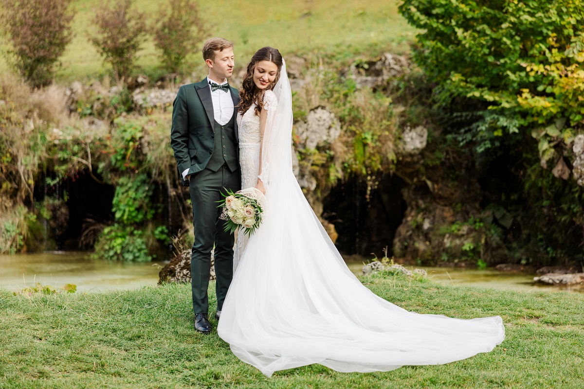 bride in white dress and groom in olive green attire posing together outdoors