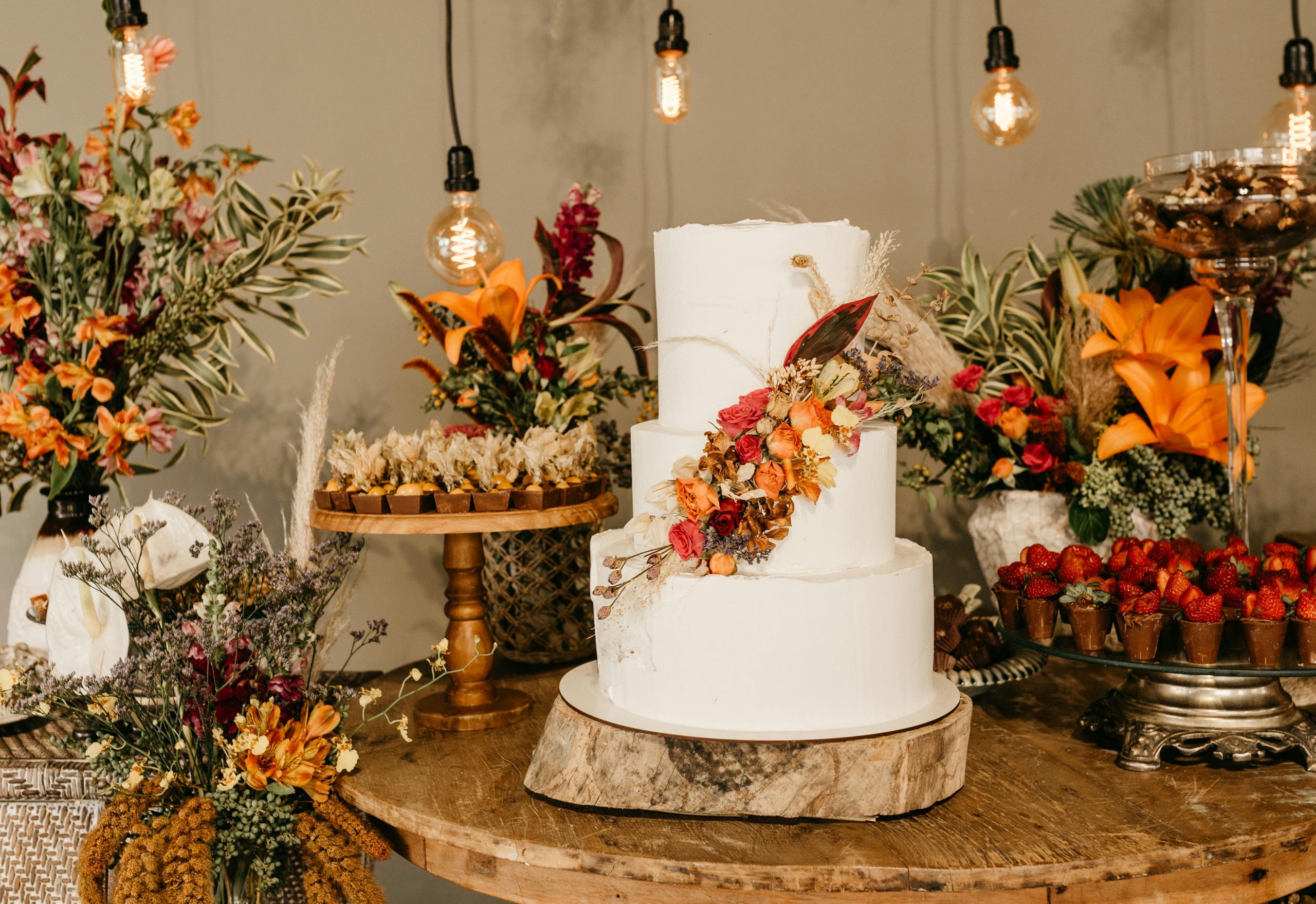 wedding cake table decorated with vibrant fall flowers and warm lights