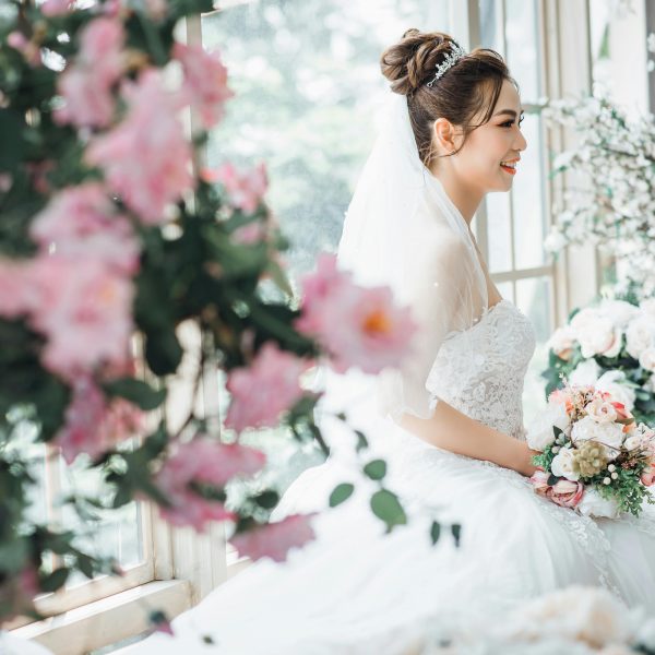 smiling bride sitting by a window, holding a bouquet of flowers