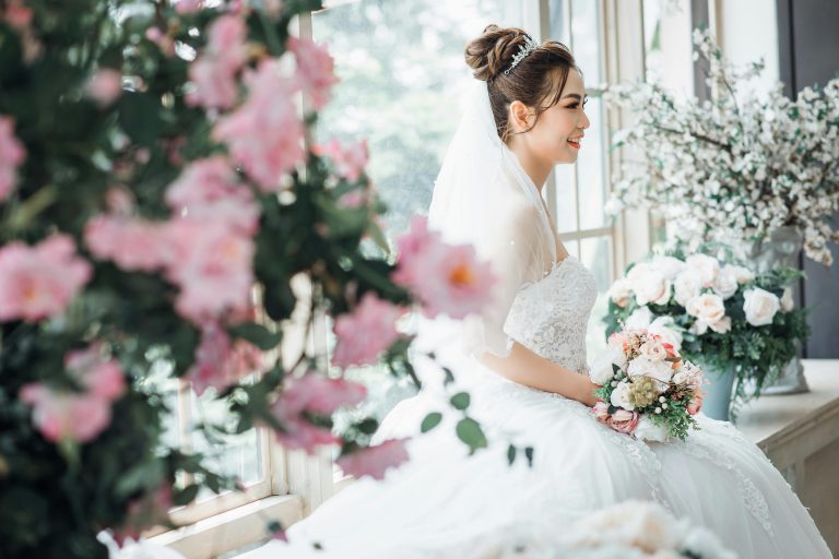 smiling bride sitting by a window, holding a bouquet of flowers